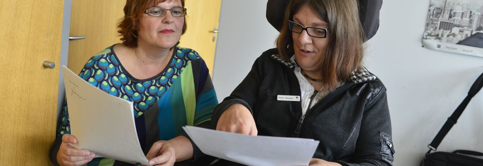 Mitarbeiterin im Rollstuhl mit ihrer Arbeitsassistenz die zusammen Unterlagen sichten